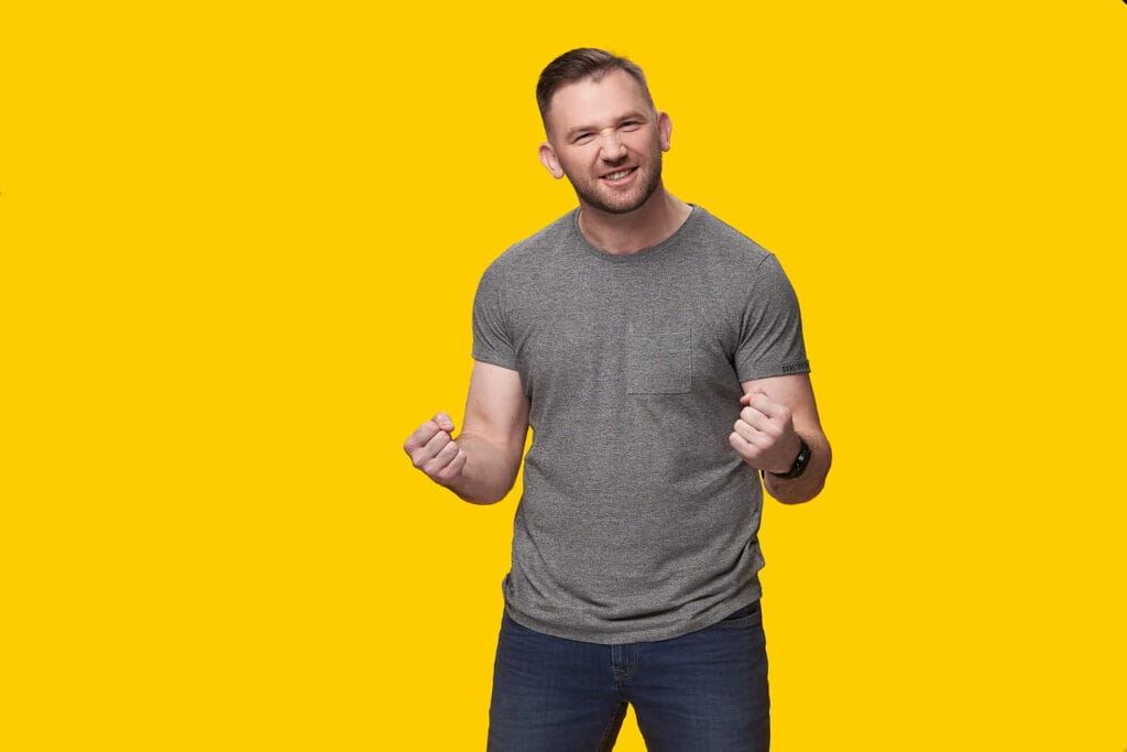 Sesja biznesowa - Mężczyzna w szarej koszulce, z uśmiechem i zaciśniętymi pięściami.